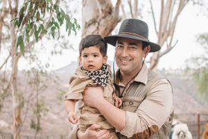Zookeeper in uniform and hat poses near eucalyptus trees at an animal park.