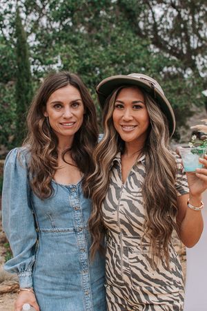 Two friends smiling together outdoors in casual wear with one wearing denim and the other in a patterned top.