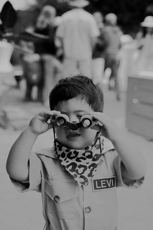 Young child wearing binoculars and a leopard print neck scarf looking through the lens.