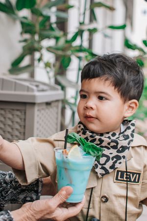 Toddler in beige outfit with leopard print bib exploring potted plants and decorations.