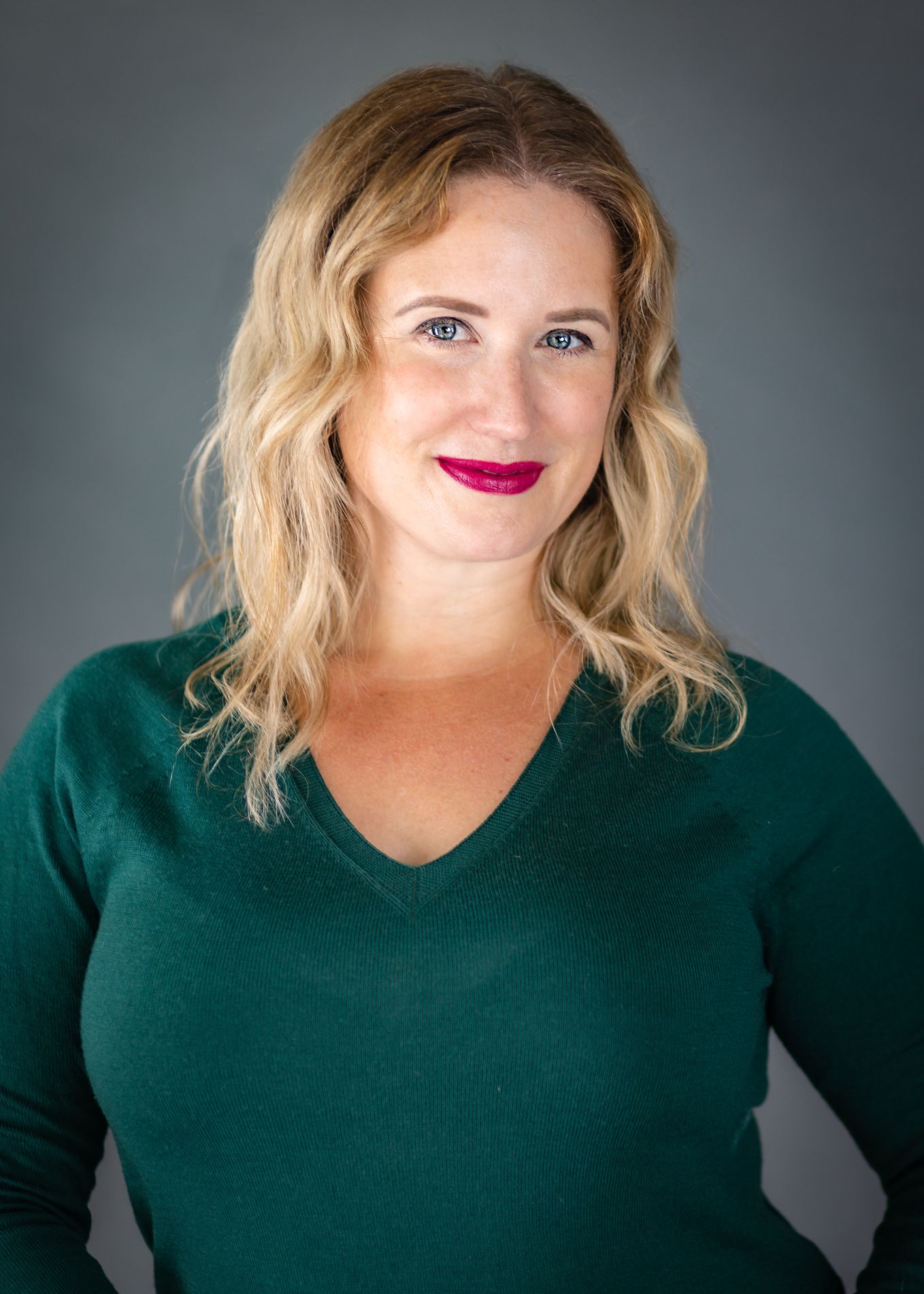 Professional headshot of person in emerald green sweater against grey background.