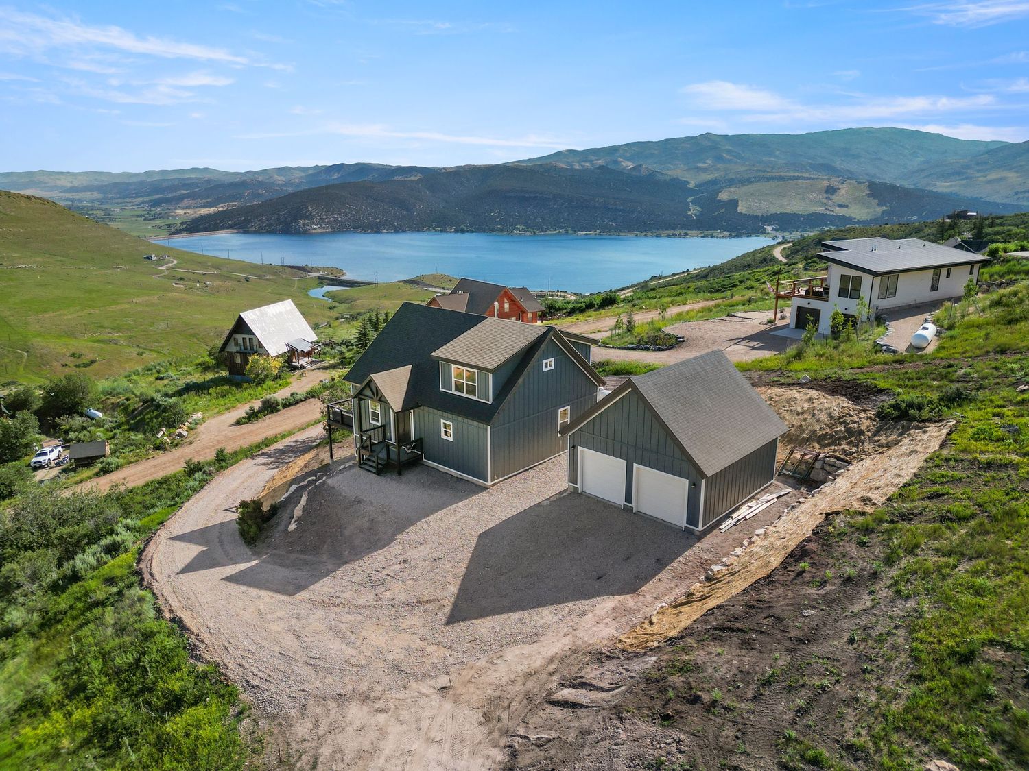 Aerial view of a large home with a two-car garage overlooking a scenic lake and rolling green hills.