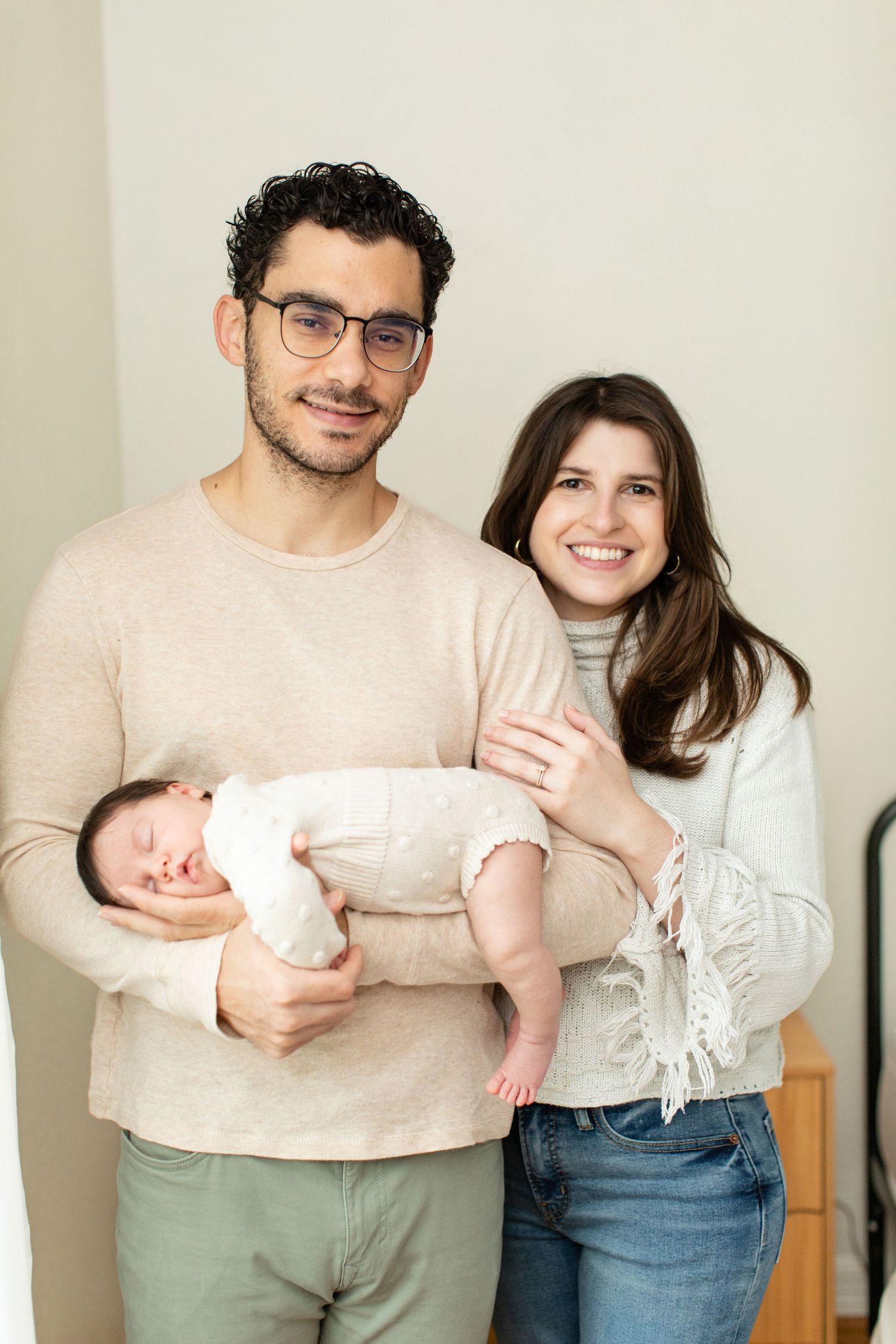 A couple poses with their newborn baby in a minimalist home setting.