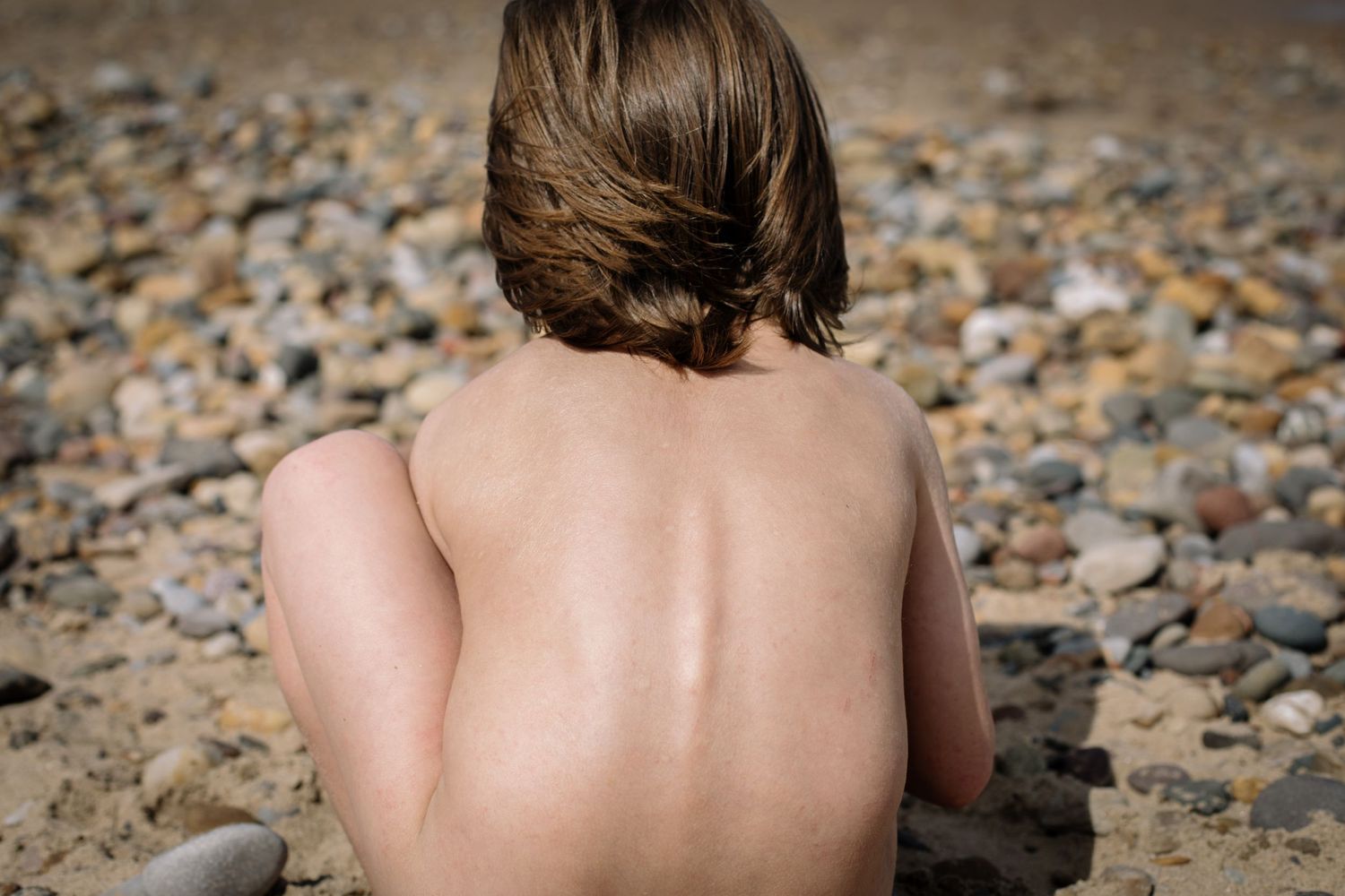 Back view of someone sitting on a rocky beach, looking at the ocean.