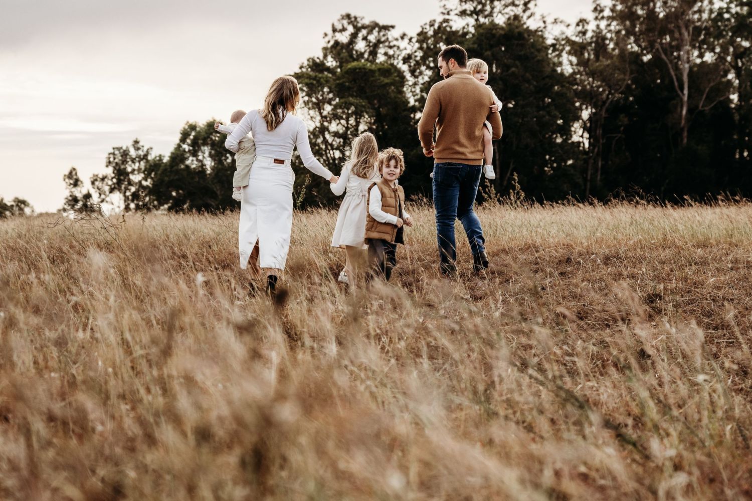 Family walking through tall grass field during overcast day.