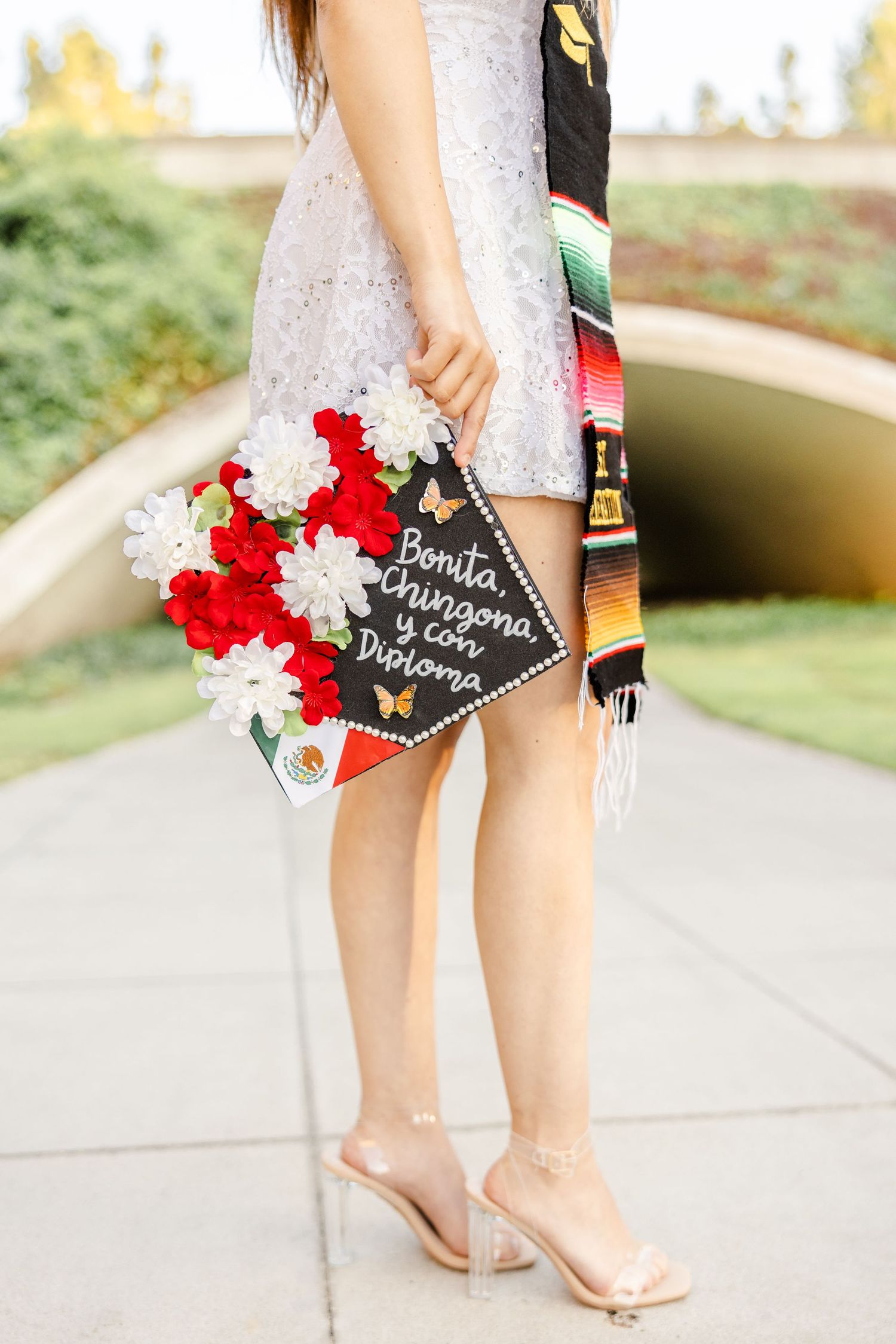 Close-up of feet in nude heels next to red and white flowers with a small chalkboard sign.