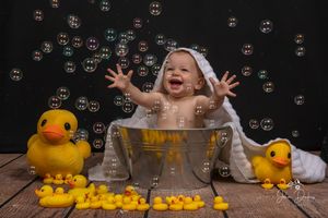 Bath tub photography setup with floating bubbles and yellow rubber ducks against black background.