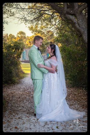 A couple shares a romantic moment at sunset under trees in their wedding attire.