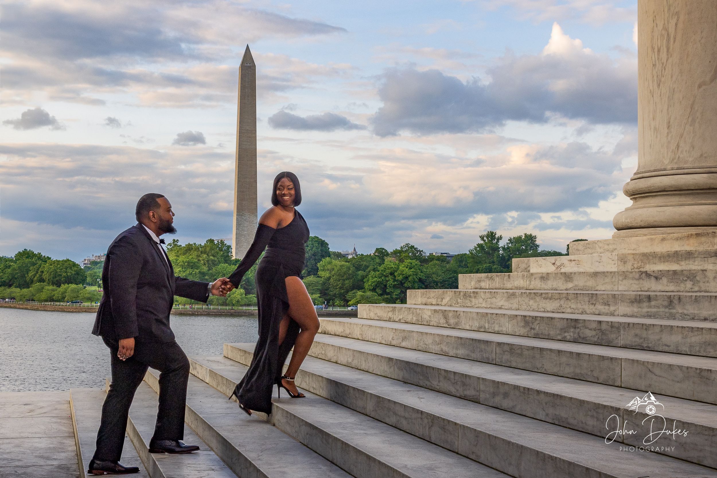 Couple posing on stone steps at sunset near waterfront columns.