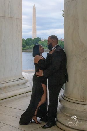 A couple shares an intimate moment between marble columns with the Washington Monument visible.