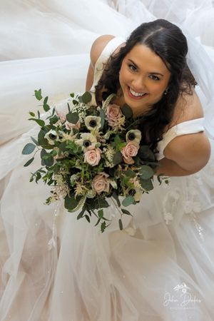 Overhead view of bride holding romantic bouquet with roses and greenery.