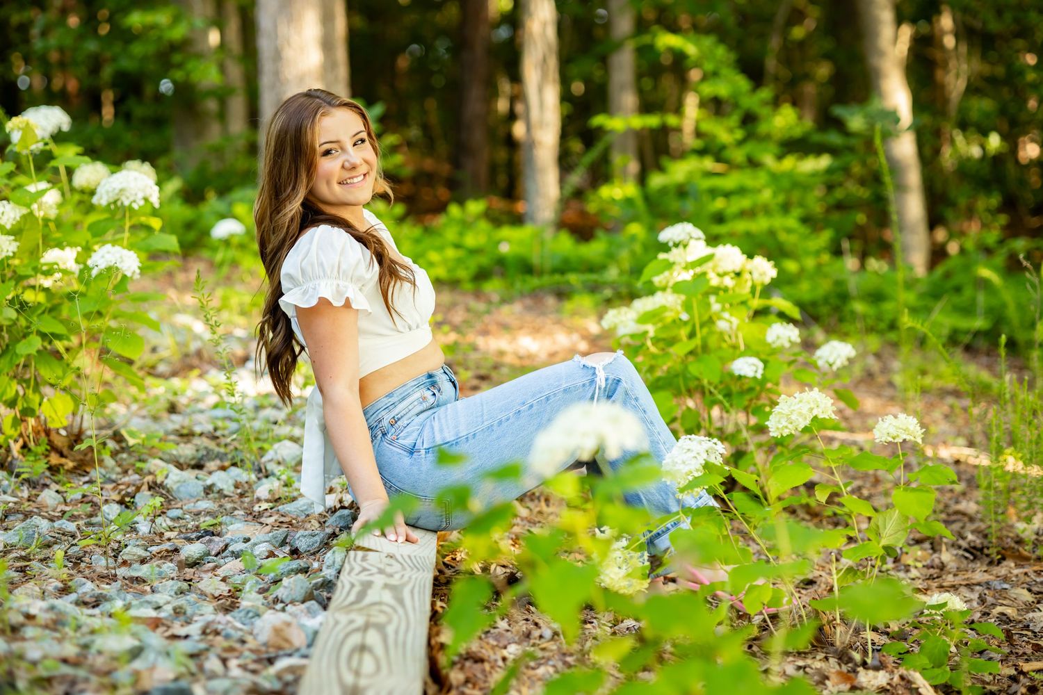 Summer fashion portrait on rustic bench surrounded by white wildflowers.