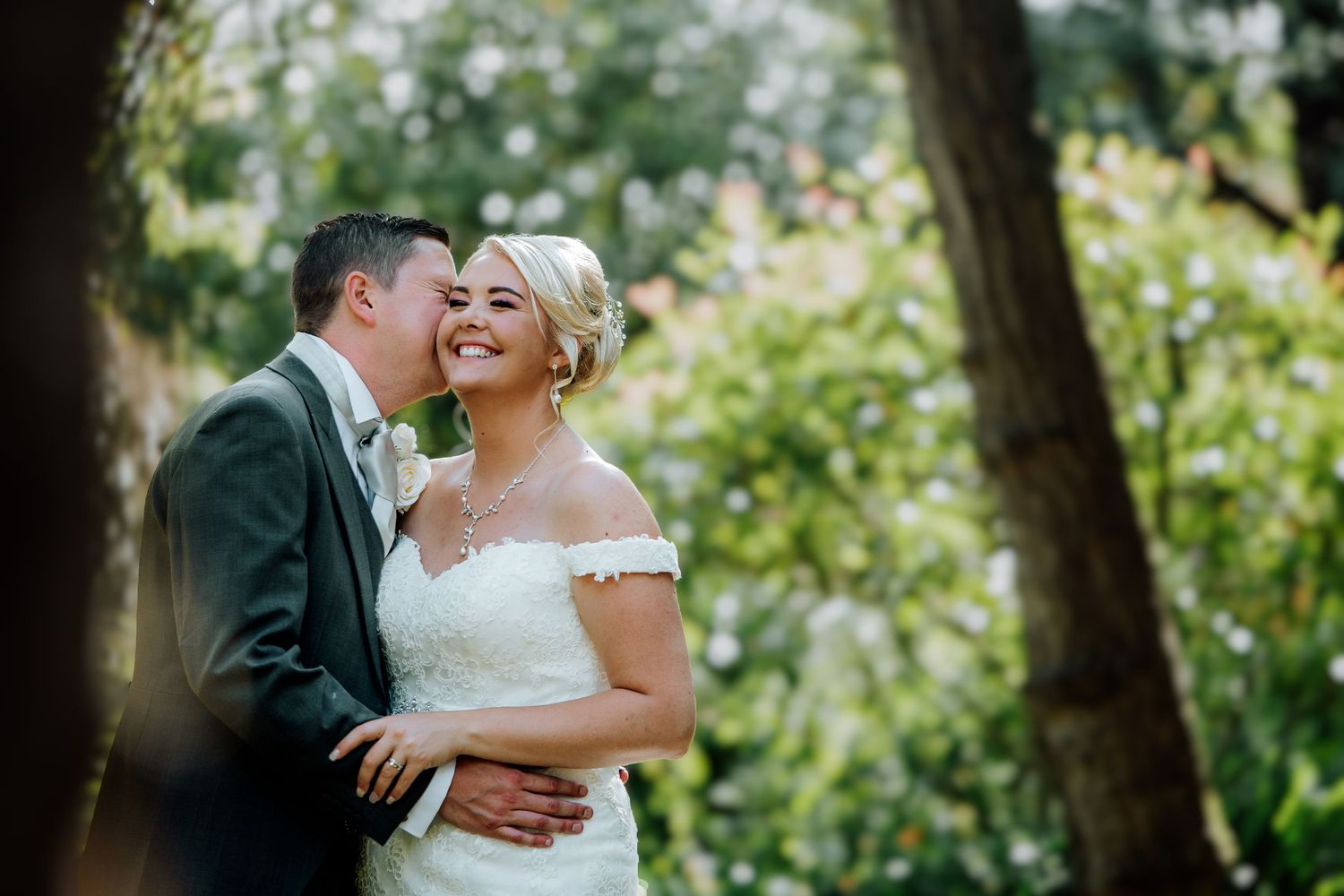 Romantic outdoor wedding portrait with couple embracing among lush greenery.