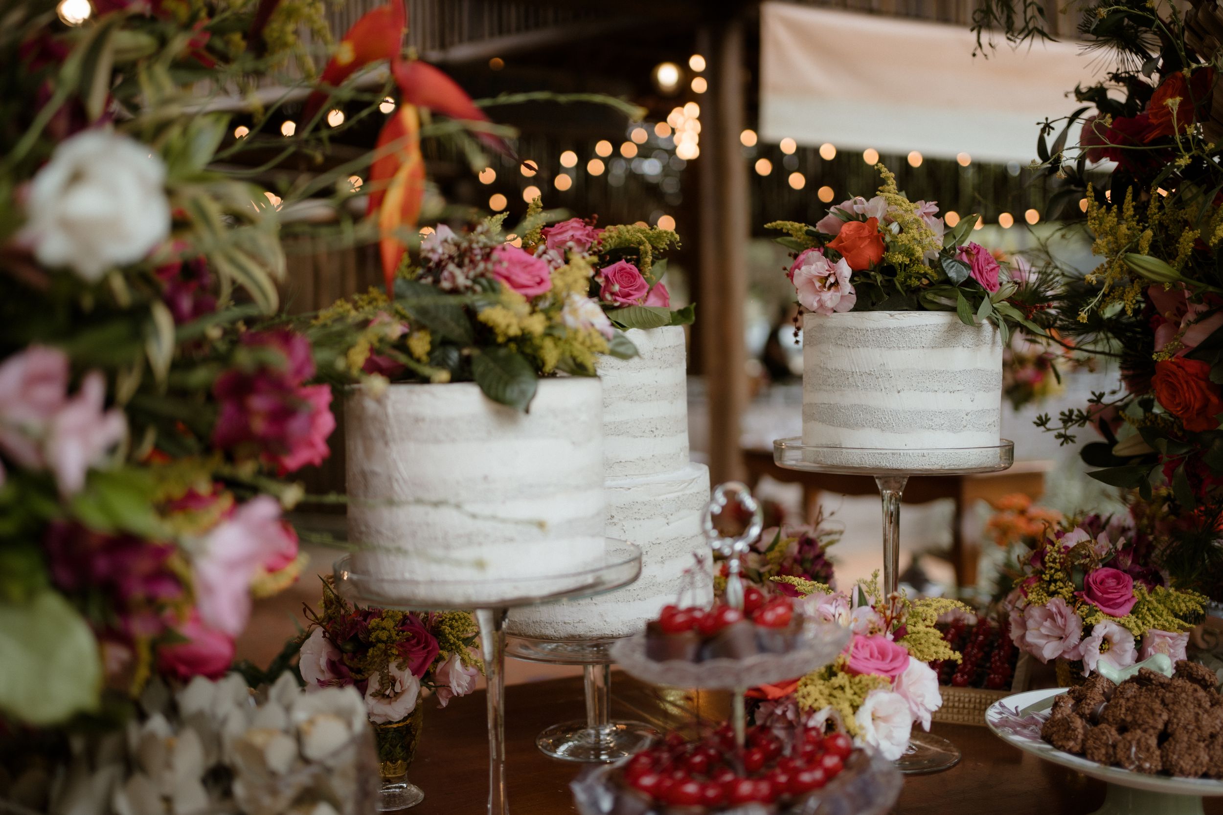 White wedding cakes decorated with fresh flowers and string lights on display.
