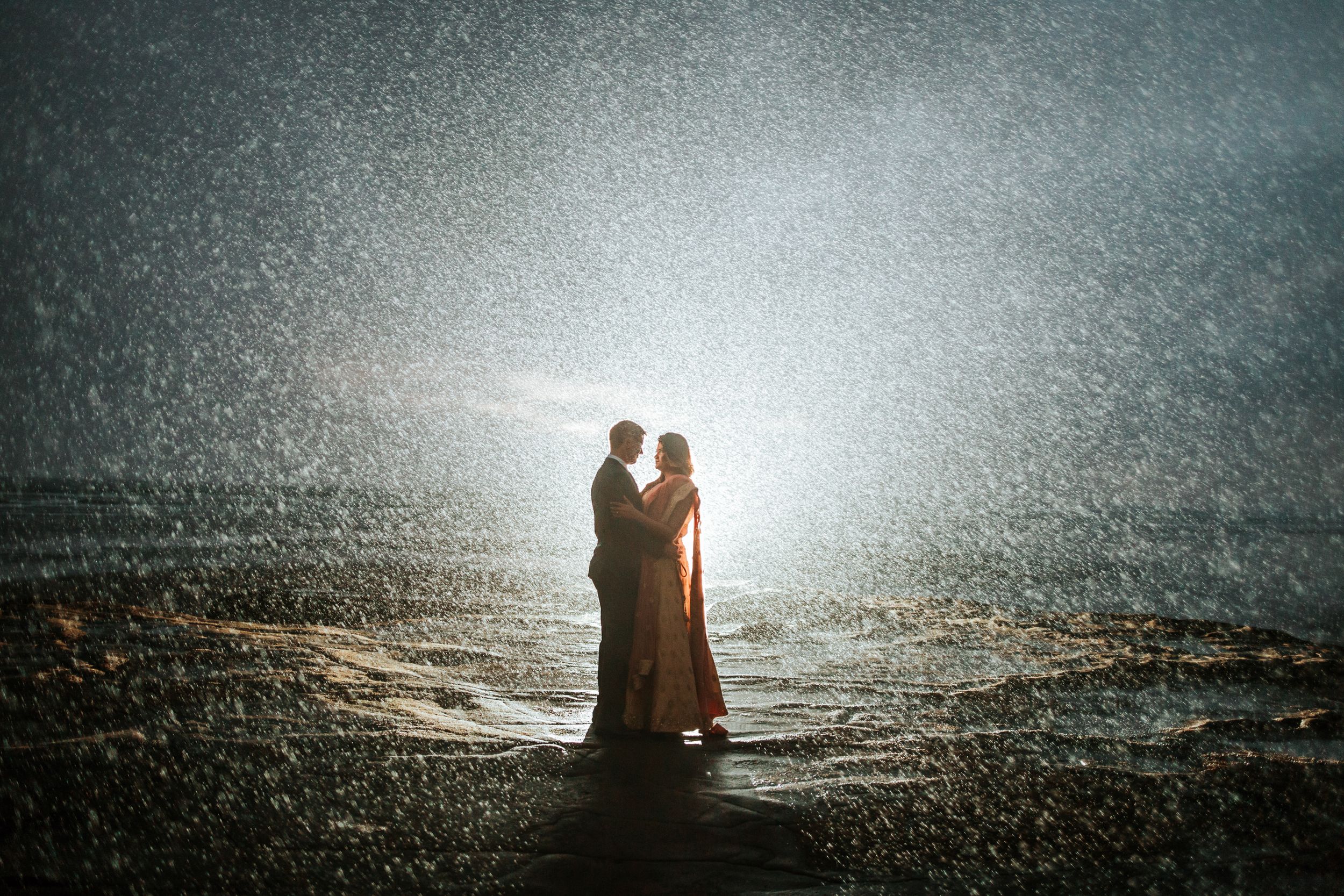 Couple posing under the rain in the evening with backlight flash Muriwai Beach Kumeu Auckland