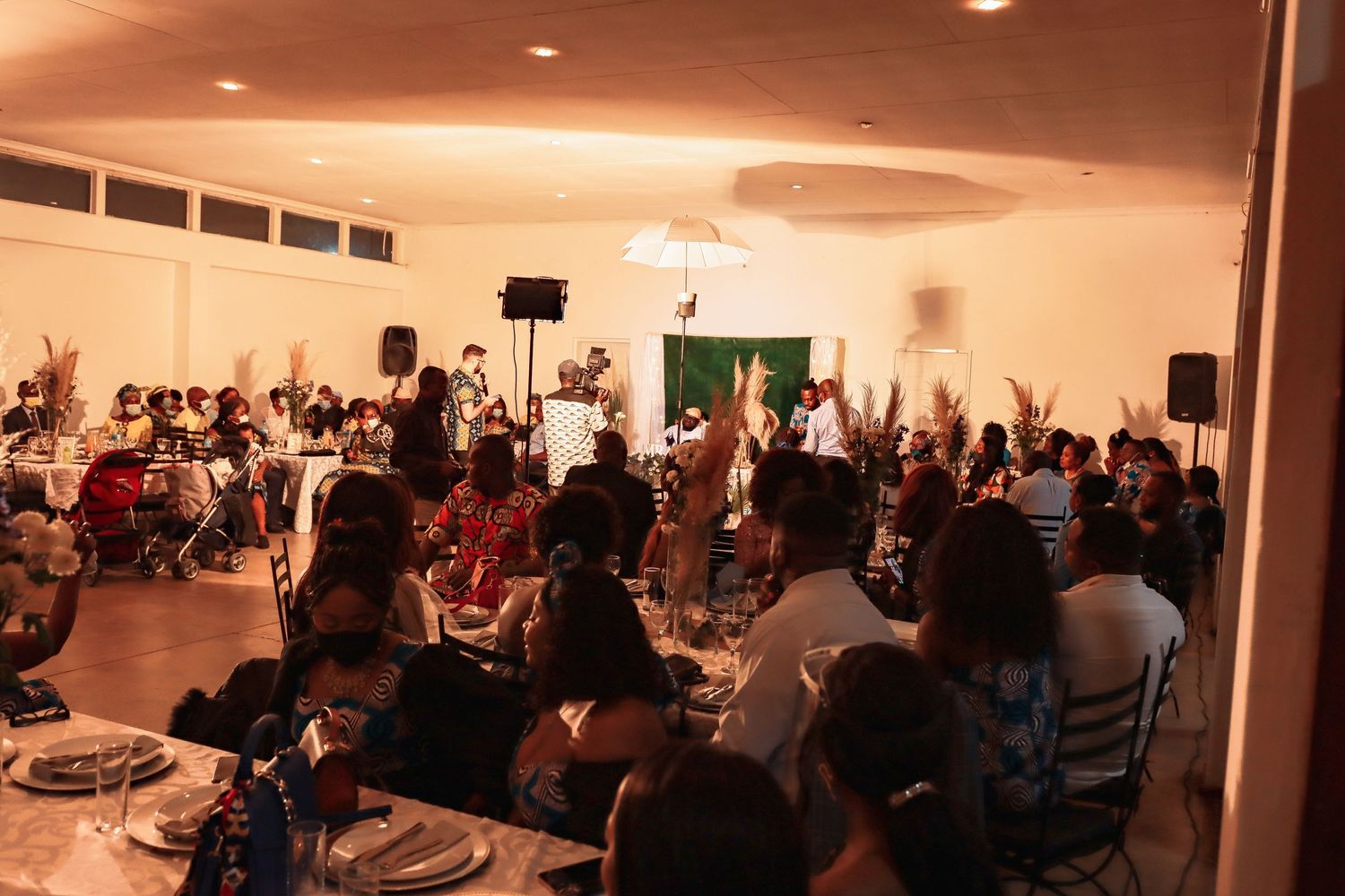 A crowded event venue with people seated at tables and large speakers set up for entertainment.