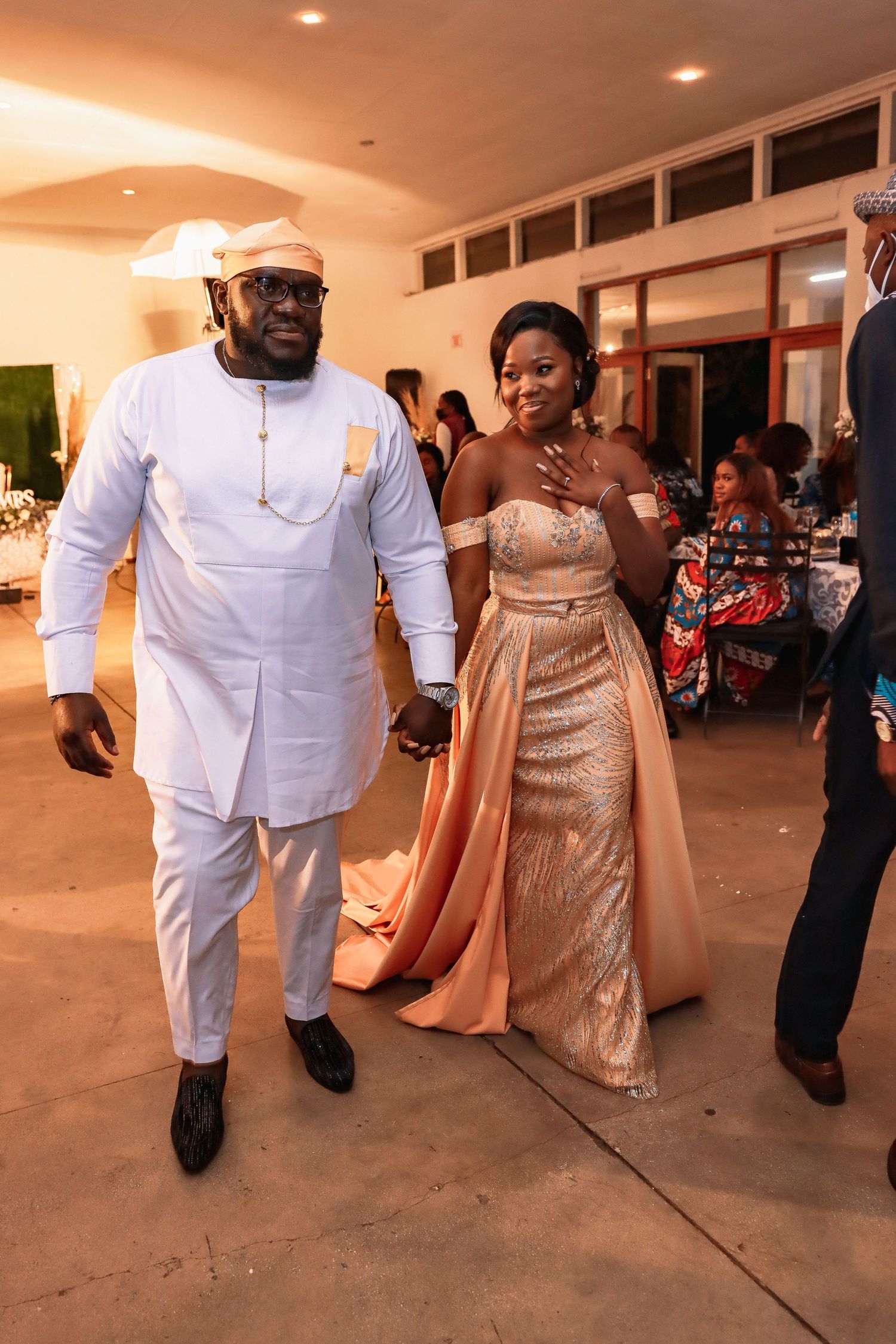 Couple in elegant white and gold formal attire walking together at an evening event.