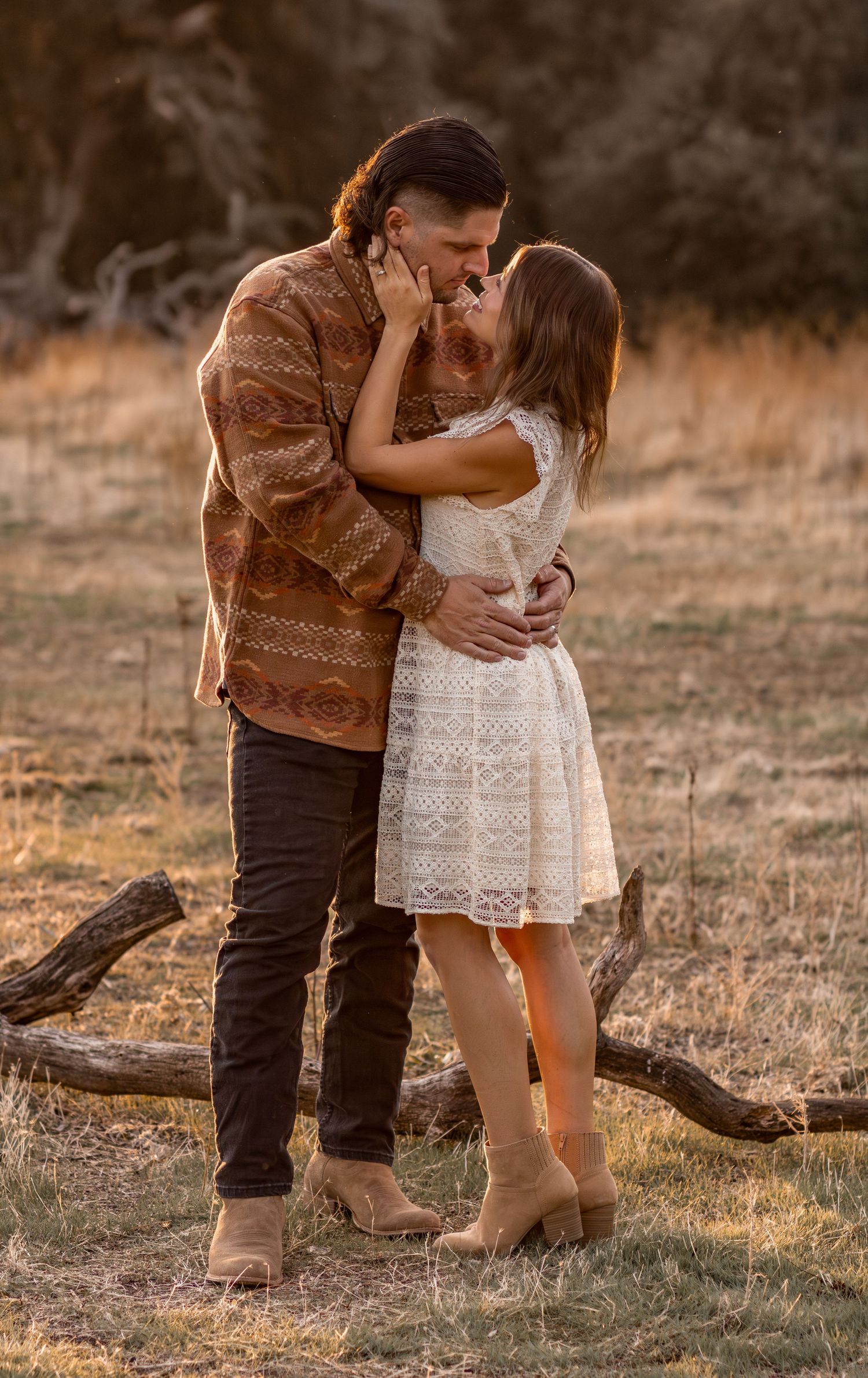 Couple sharing a romantic kiss in golden hour light in a rustic dry grass field.