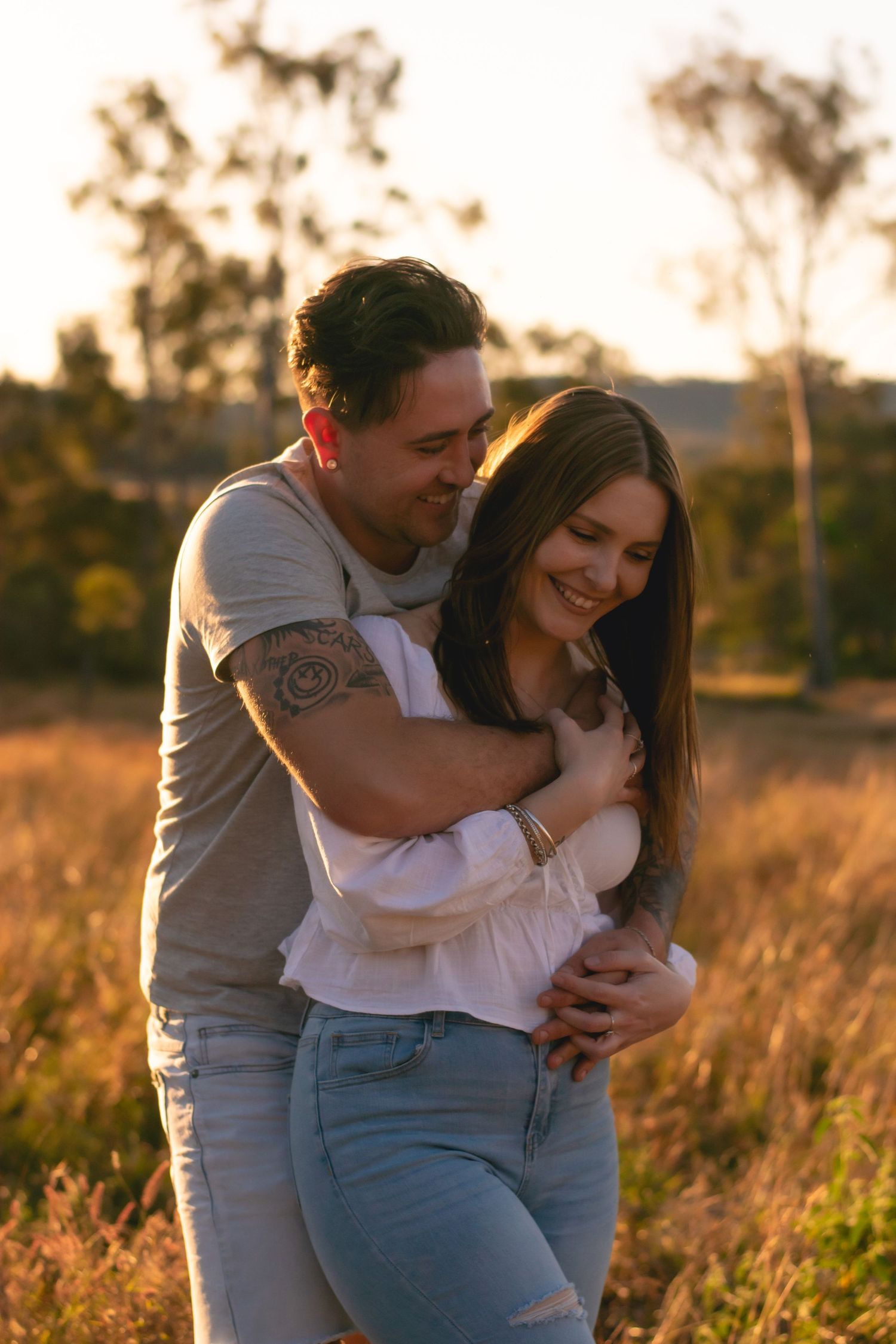 Couple embracing and laughing together in a sun-lit field at golden hour.