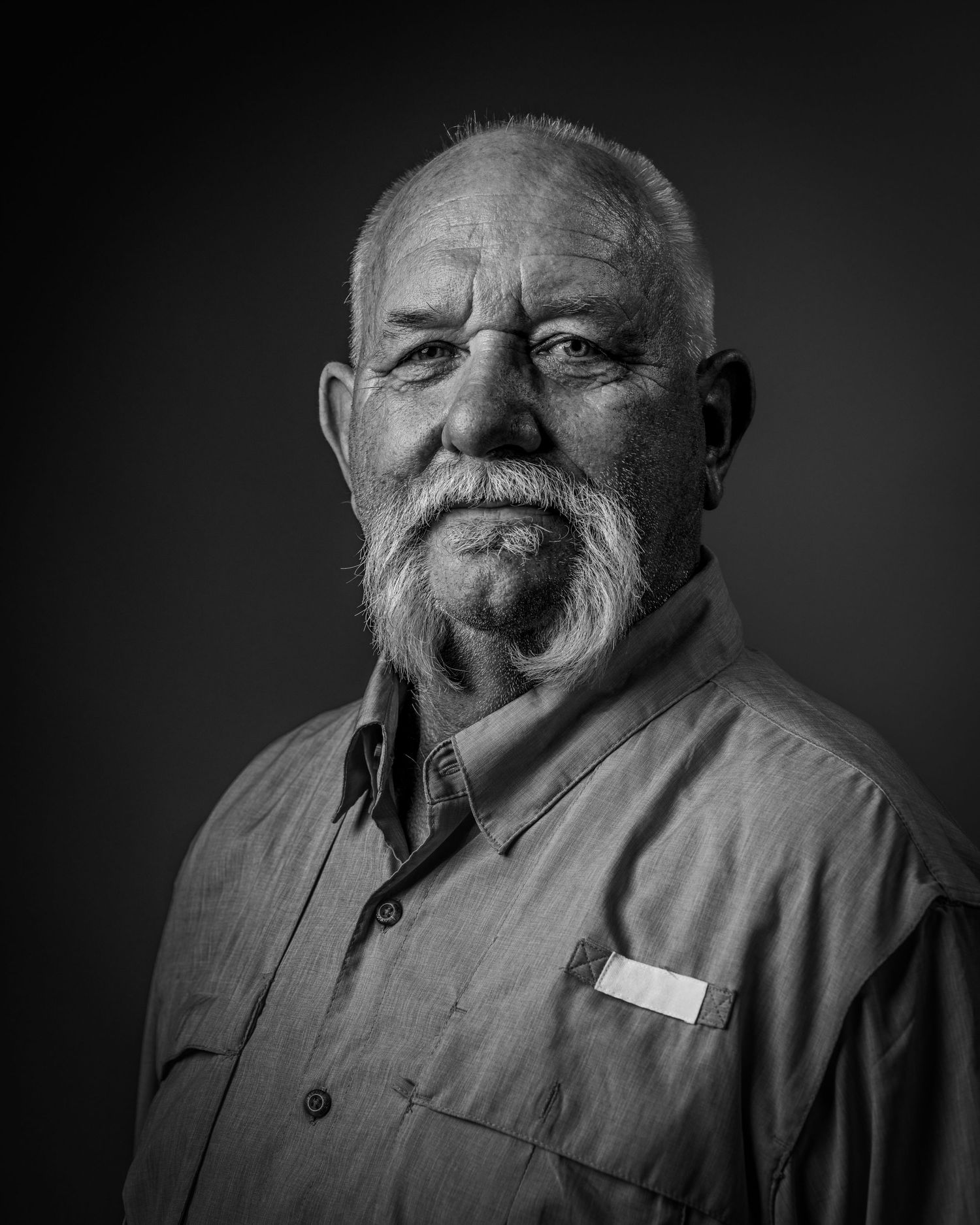 Black and white portrait against dark background in dramatic lighting.