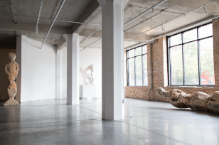 Modern gallery space with concrete floors, white walls and large industrial windows.