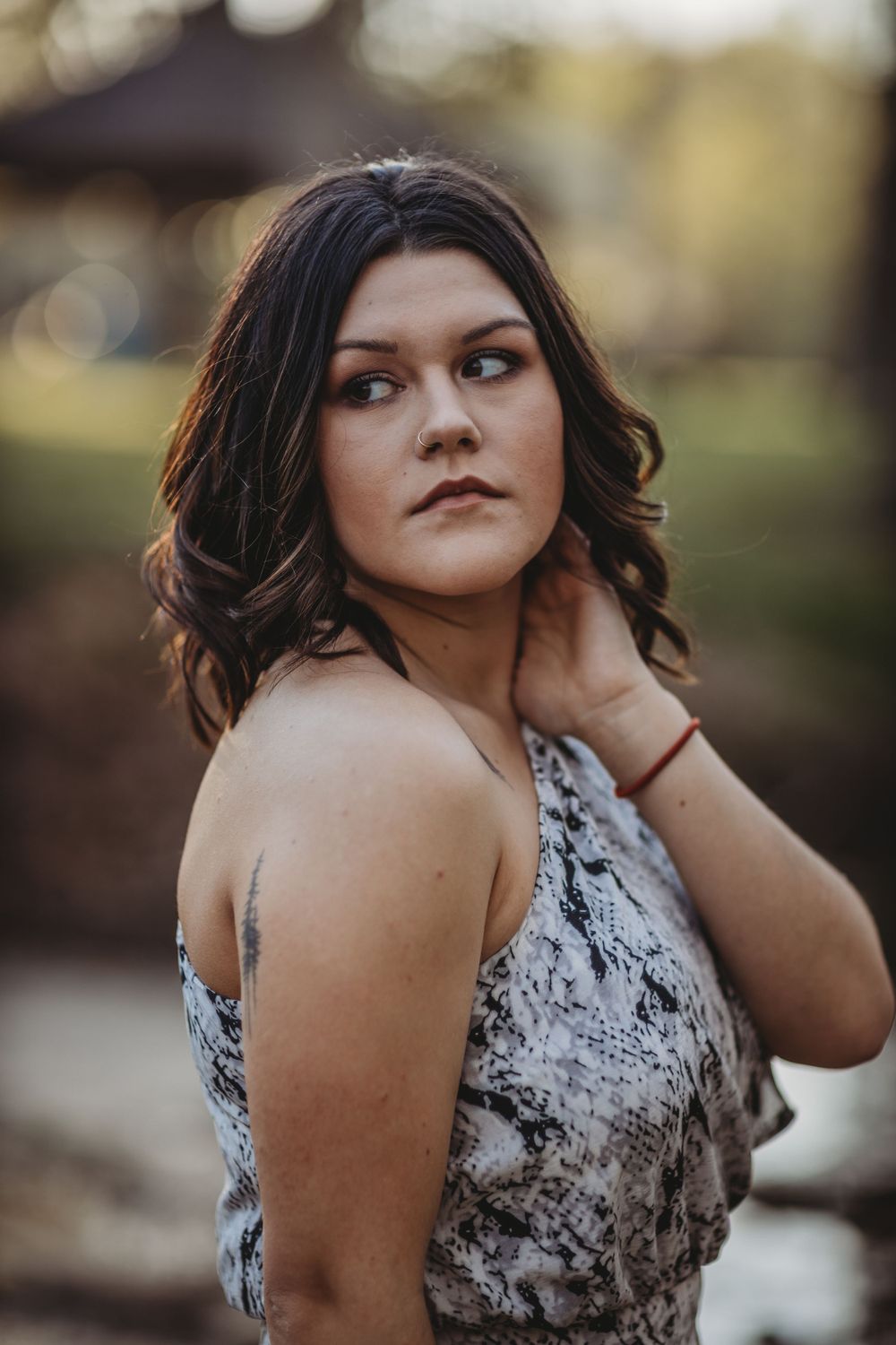 Young woman in snake print dress poses outdoors during golden hour, hand touching neck.