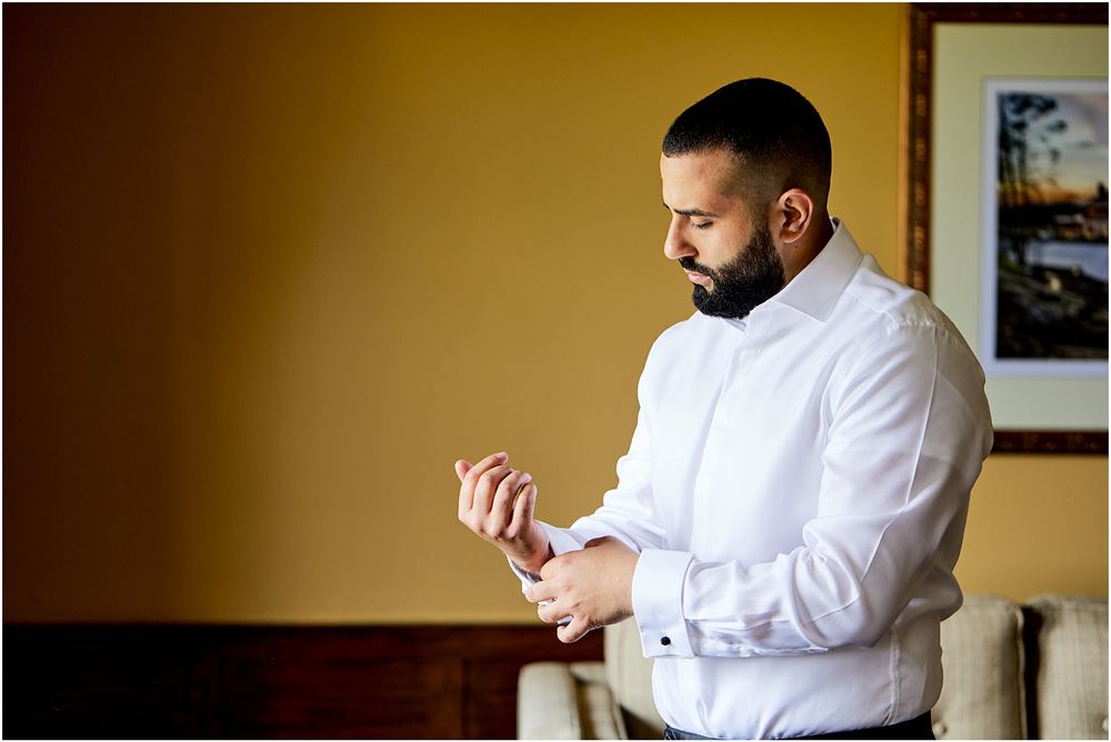 Man in white dress shirt adjusting cufflinks in warm indoor lighting.