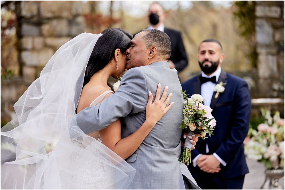 Romantic wedding ceremony kiss with floral arrangements and stone architecture.