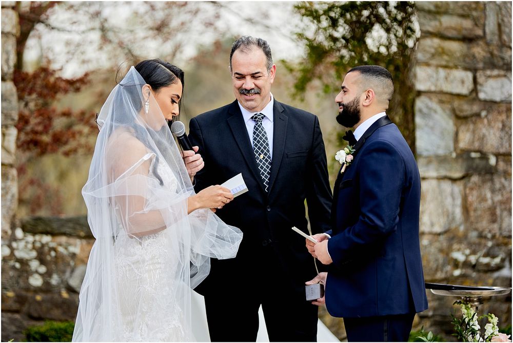 Outdoor wedding ceremony with officiant and couple in front of stone architecture.