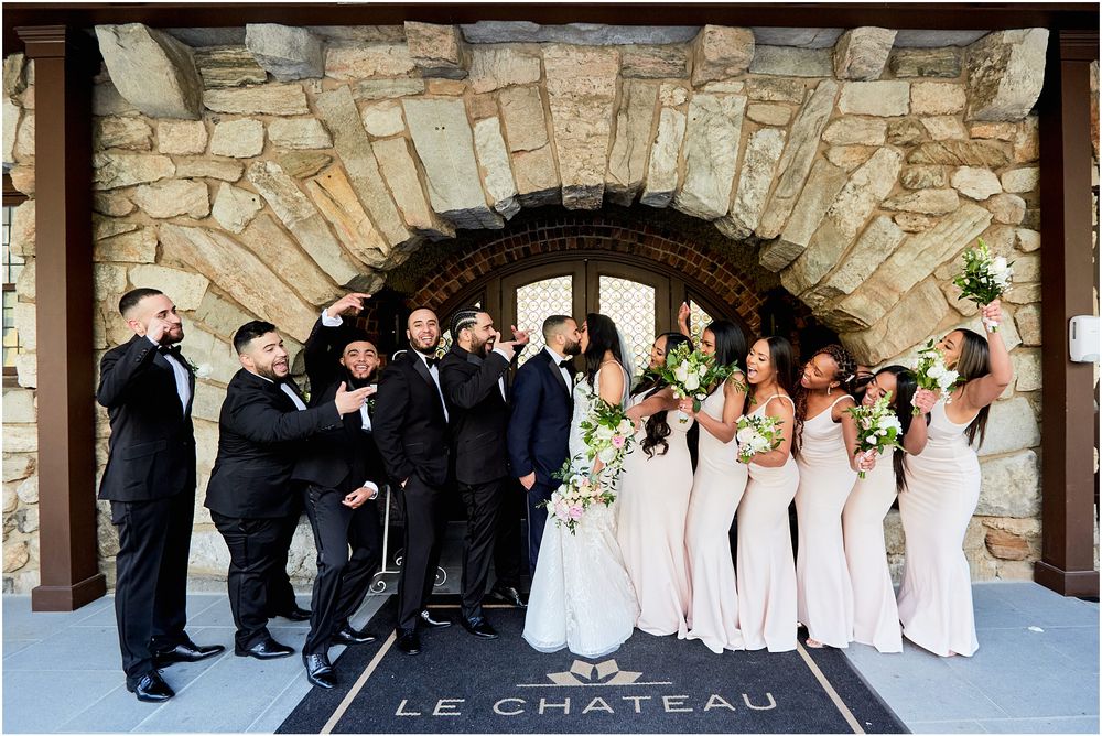 Wedding party posed under stone archway with bridesmaids in blush and groomsmen in black.