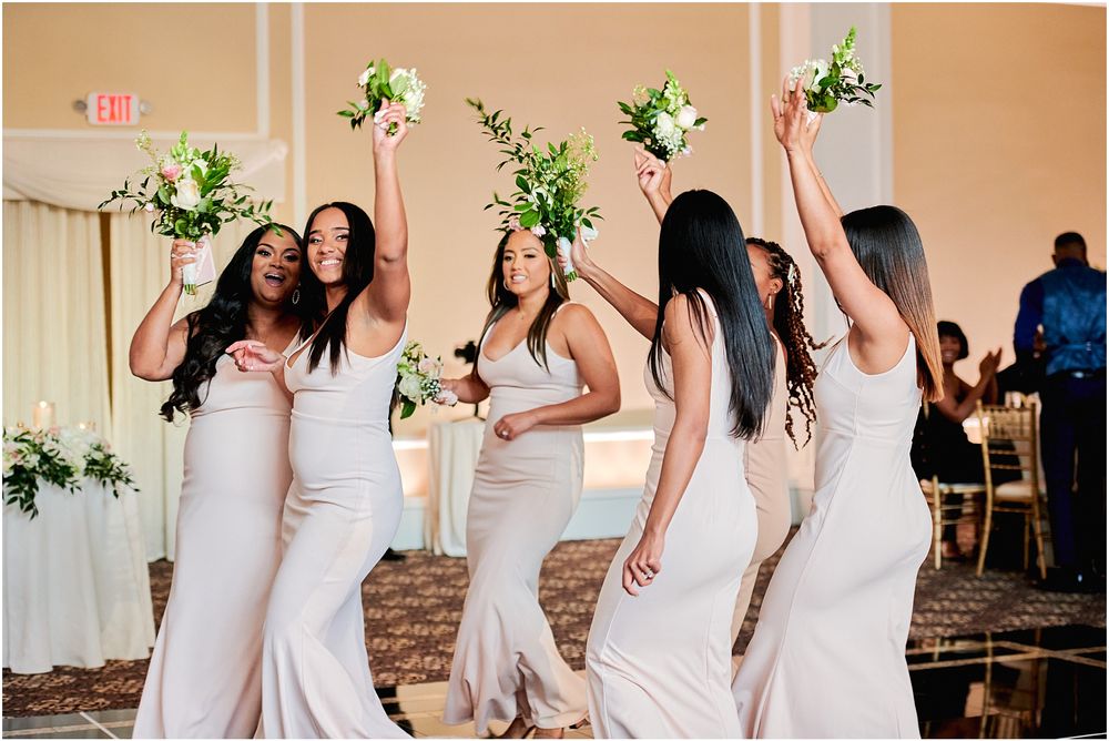 Bridesmaids in matching white dresses celebrate joyfully with bouquets at an elegant wedding reception.