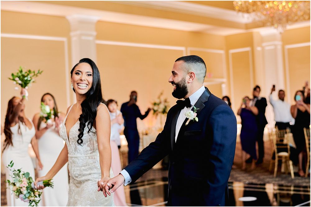 Couple shares a romantic moment on their wedding day in an elegant ballroom with chandelier.
