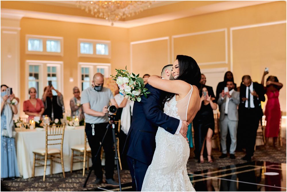 Wedding couple shares their first dance surrounded by guests in an elegant ballroom setting.