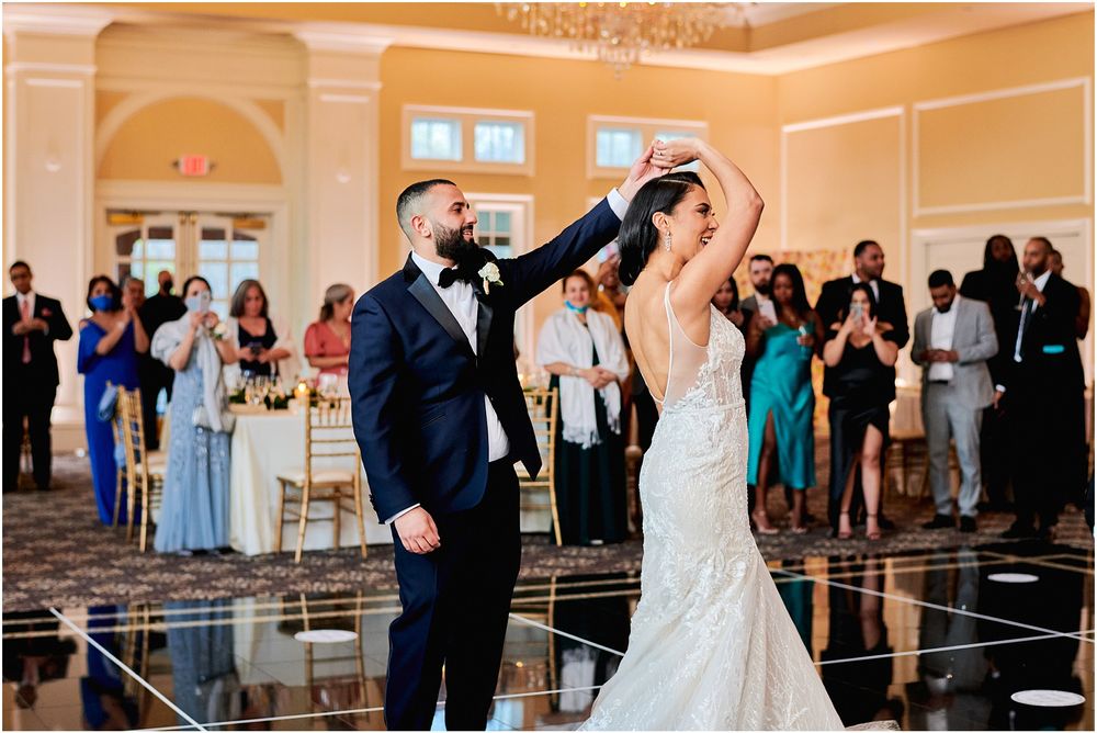 Couple performs an elegant dance twirl on a reflective black dance floor at their wedding reception.