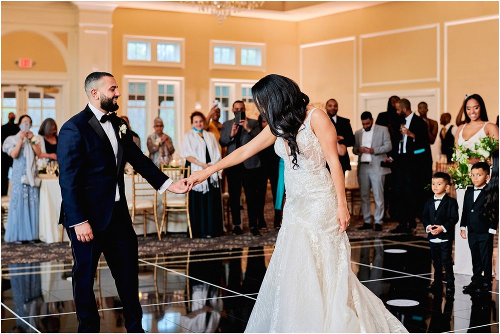 Couple performs energetic dance moves on a reflective floor during their wedding reception.