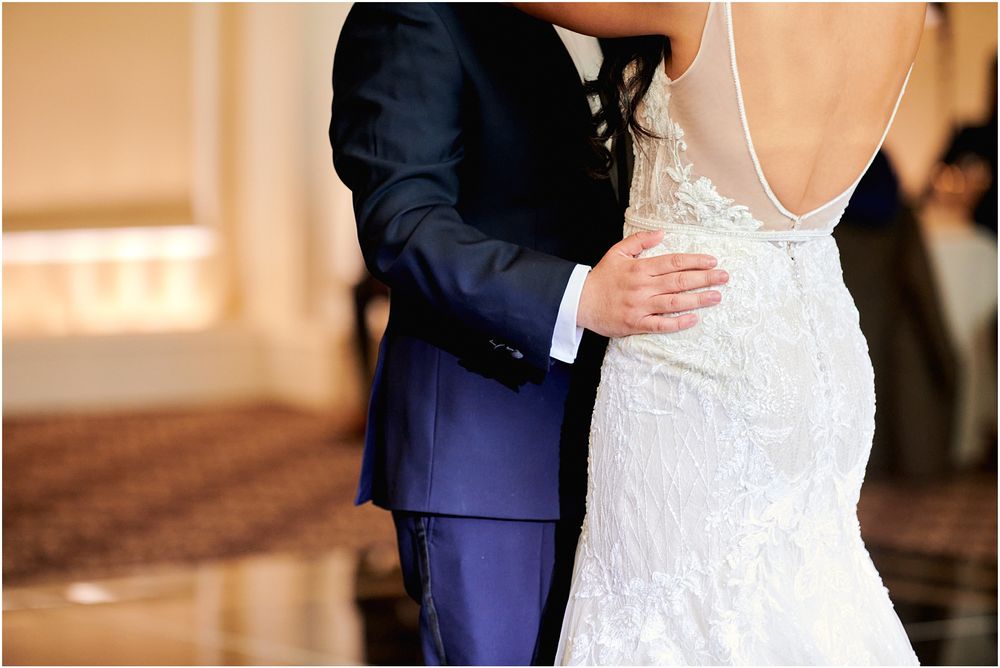 Close-up detail of wedding couple embracing, showing intricate lace details of bridal gown.