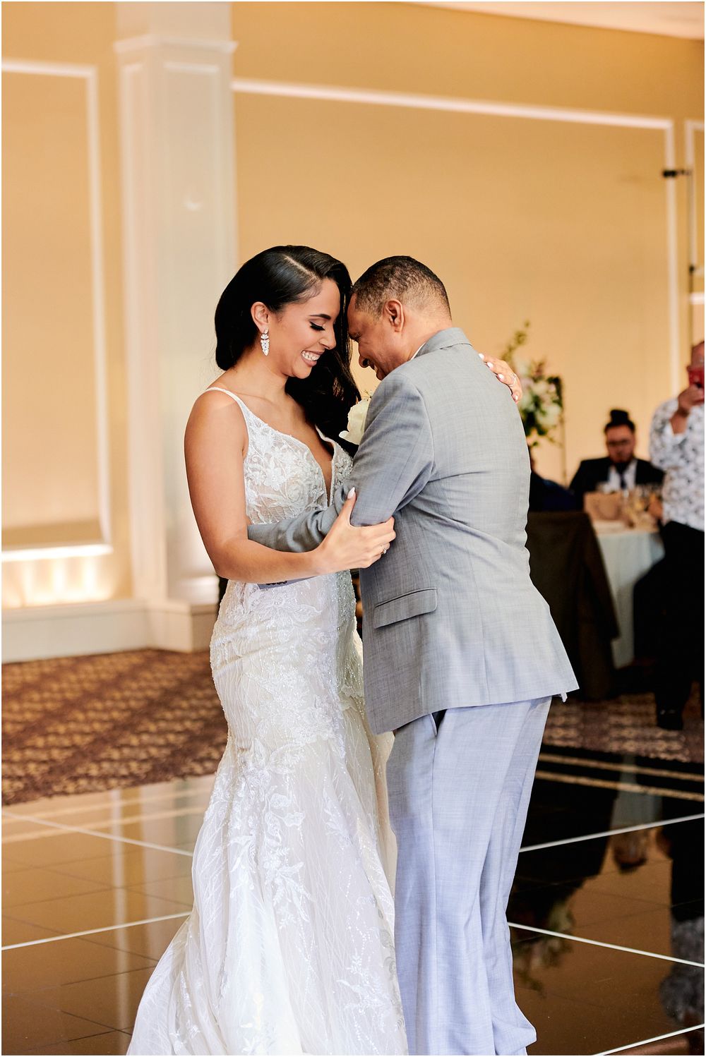 A couple shares their first dance at a wedding reception in an elegant ballroom with reflective flooring.