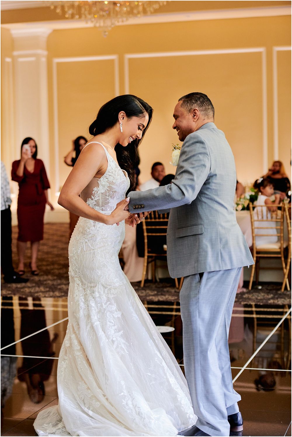 Newlyweds dance together in an elegant ballroom with warm lighting and decorative walls.