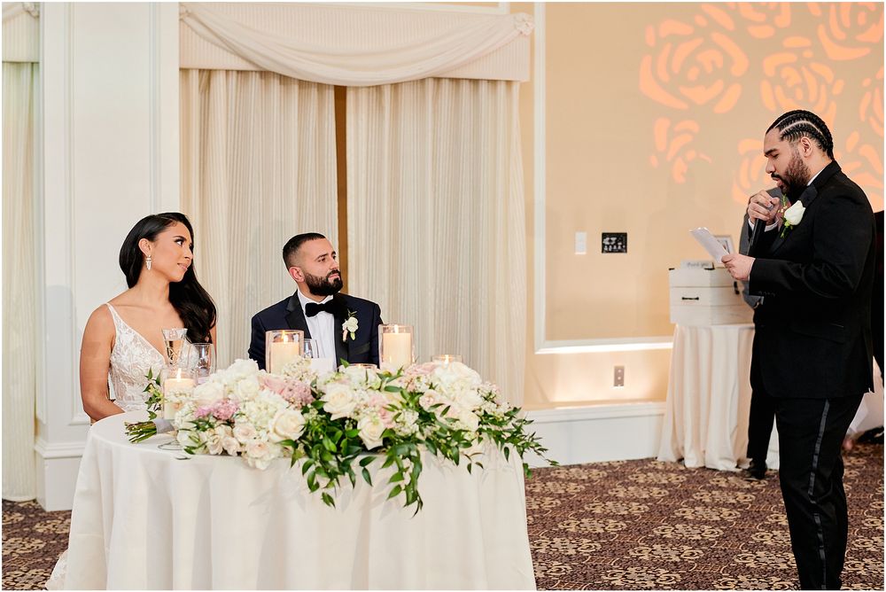 Wedding reception scene with sweetheart table featuring lush white floral arrangements and elegant draping.