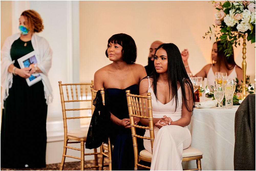 Wedding guests in formal attire seated at reception tables with elegant gold chairs.