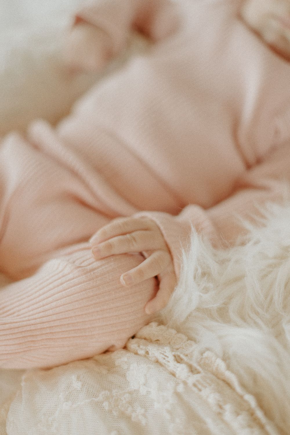 Close-up detail of tiny fingers grasping soft pink ribbed fabric against white lace.