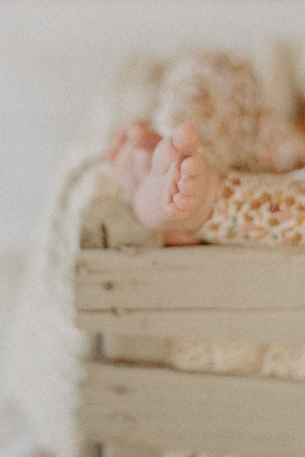 Close-up of tiny baby feet resting on vintage wooden crate with lace detail.