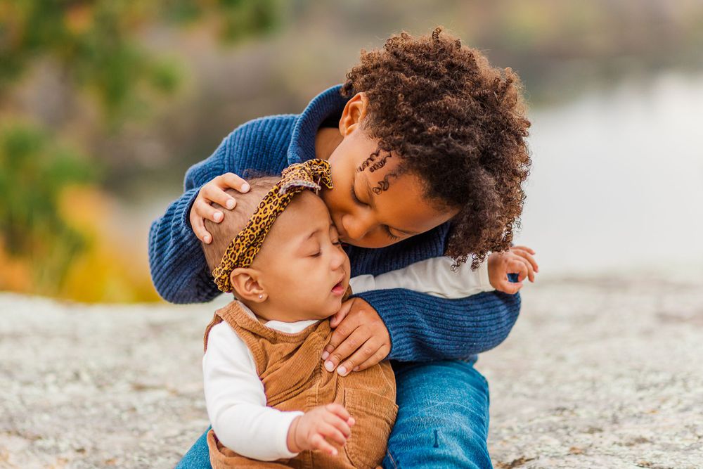 Tender moment between siblings sharing an embrace against natural background.