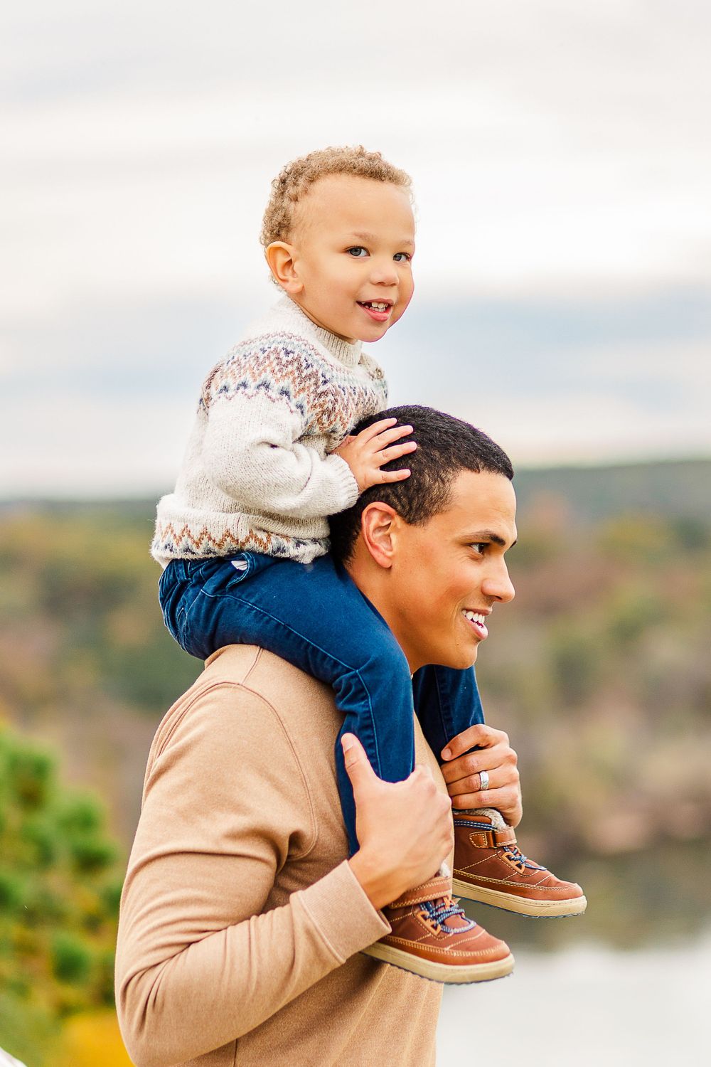 Happy moment captured as child rides on adult's shoulders against scenic autumn backdrop.