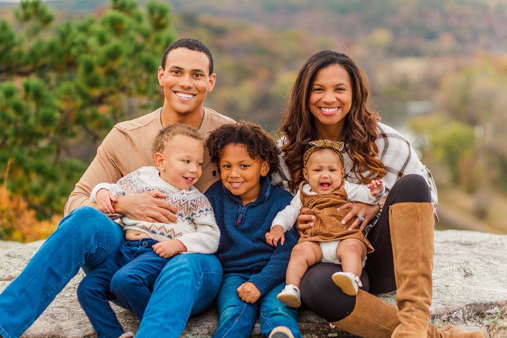 Family of five poses together on rocky overlook during fall season.