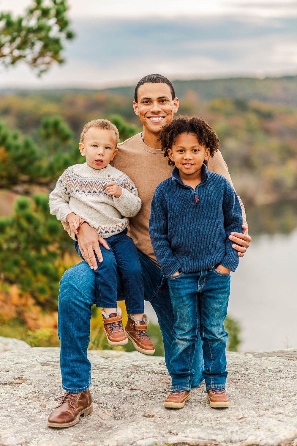 Family portrait of three people in casual wear standing on rocky overlook during autumn.