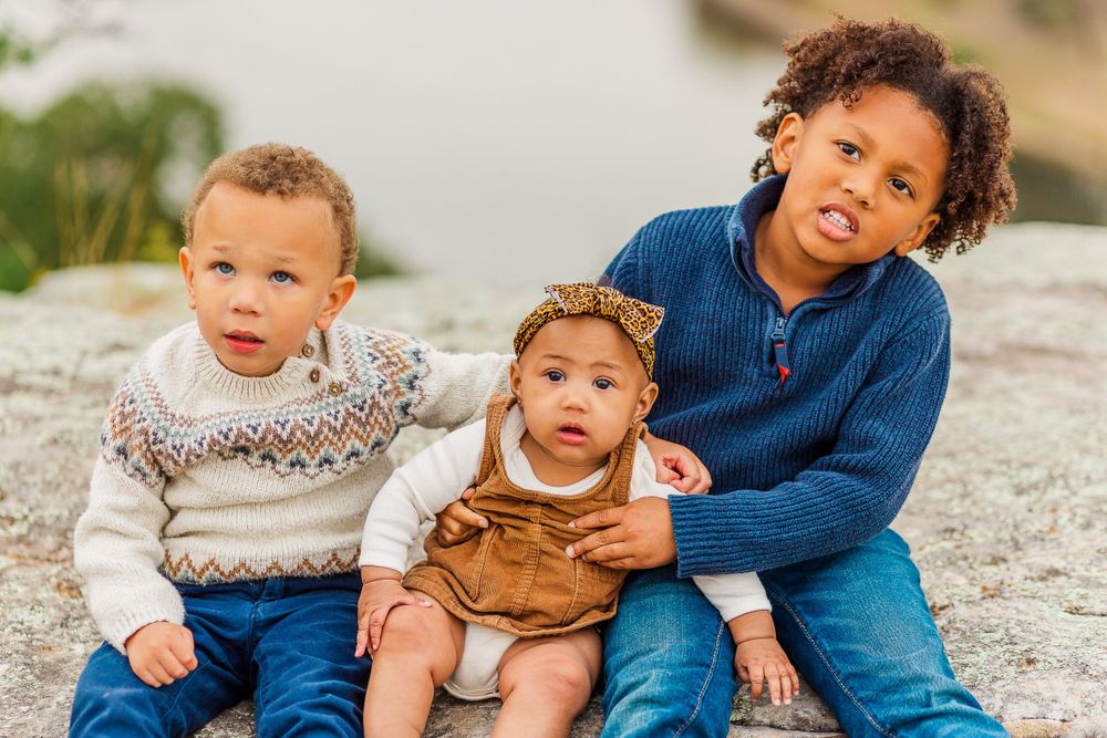 Three siblings sitting together on rocky terrain during autumn family photoshoot.