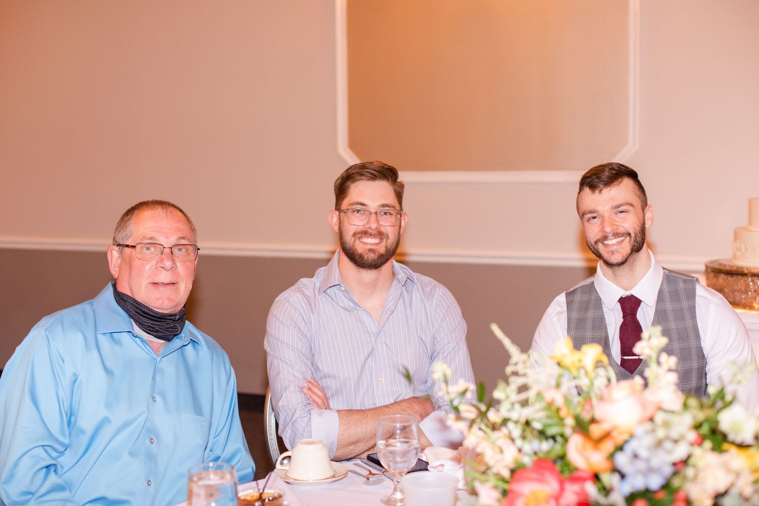 Wedding reception guests seated at long tables decorated with floral centerpieces and white linens.