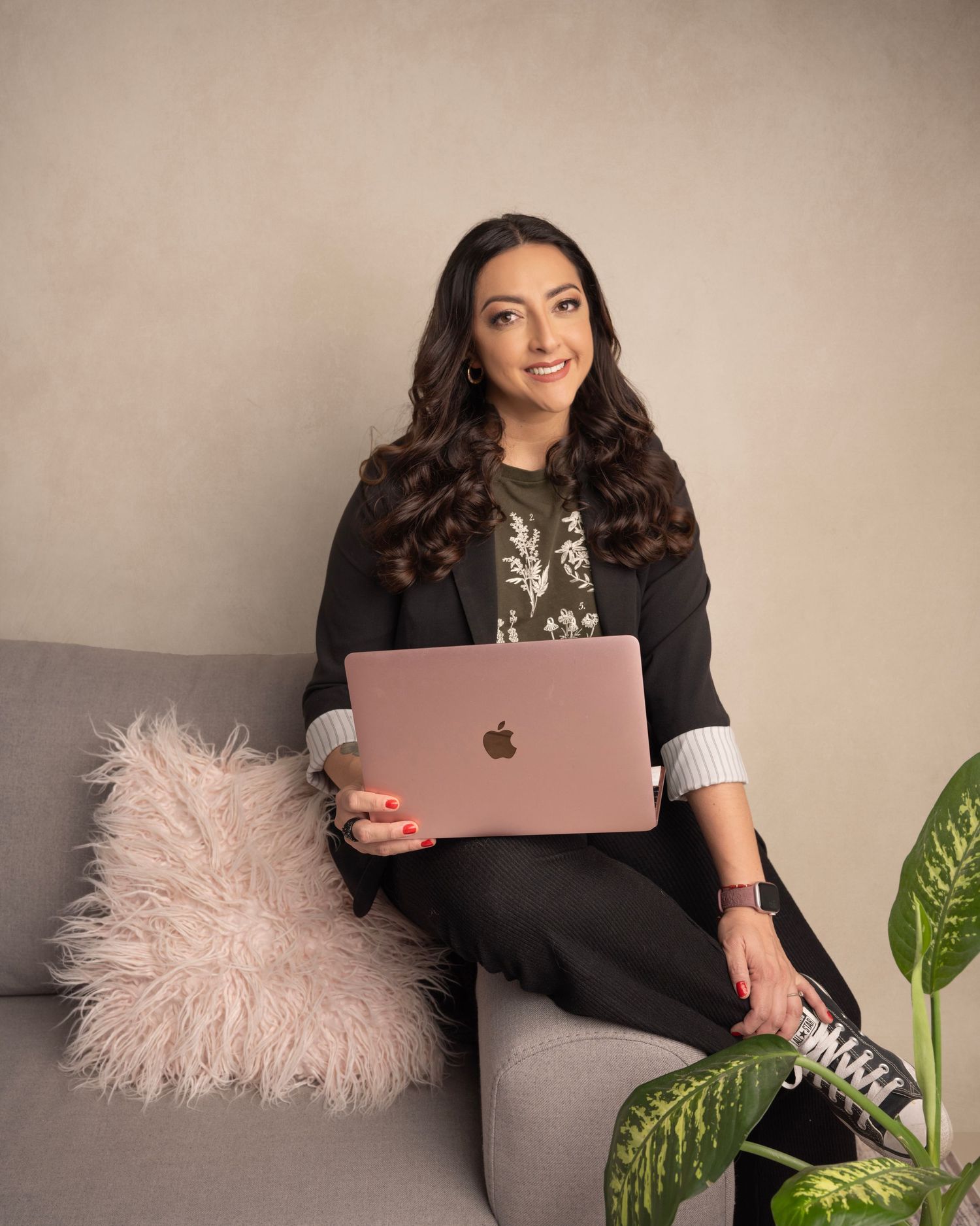 Modern lifestyle photo with casual business attire and laptop on grey couch with pink cushion.