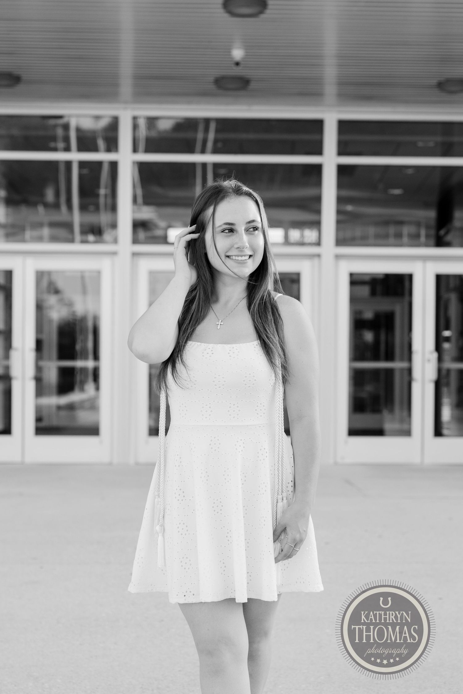 Black and white portrait of graduate standing in front of modern building entrance.
